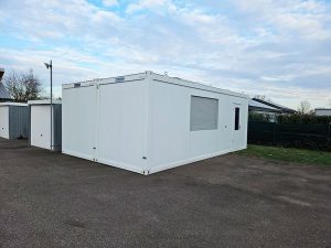 Weiße Containeranlage von Neubach Container – zwei verbundene Module mit Fenster, Rollladen und Tür auf Außenfläche