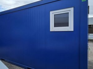 Seitenansicht eines blauen Containers mit kleinem Fenster im weißen Rahmen auf Außenstellfläche